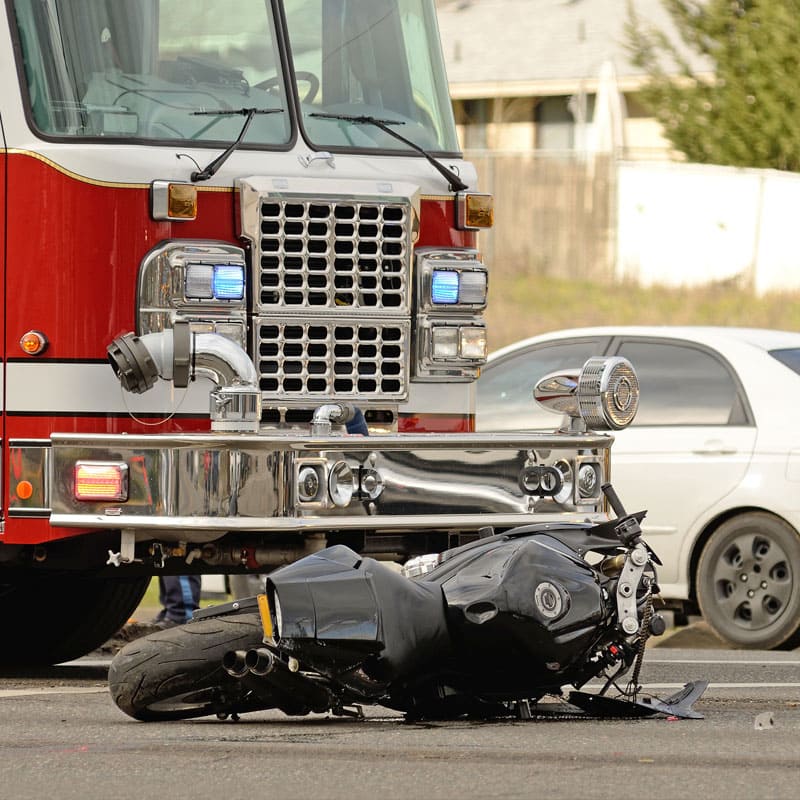 Motorcycle on its side in road with firetruck behind it